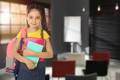 Image of Little girl with school stationery in empty classroom