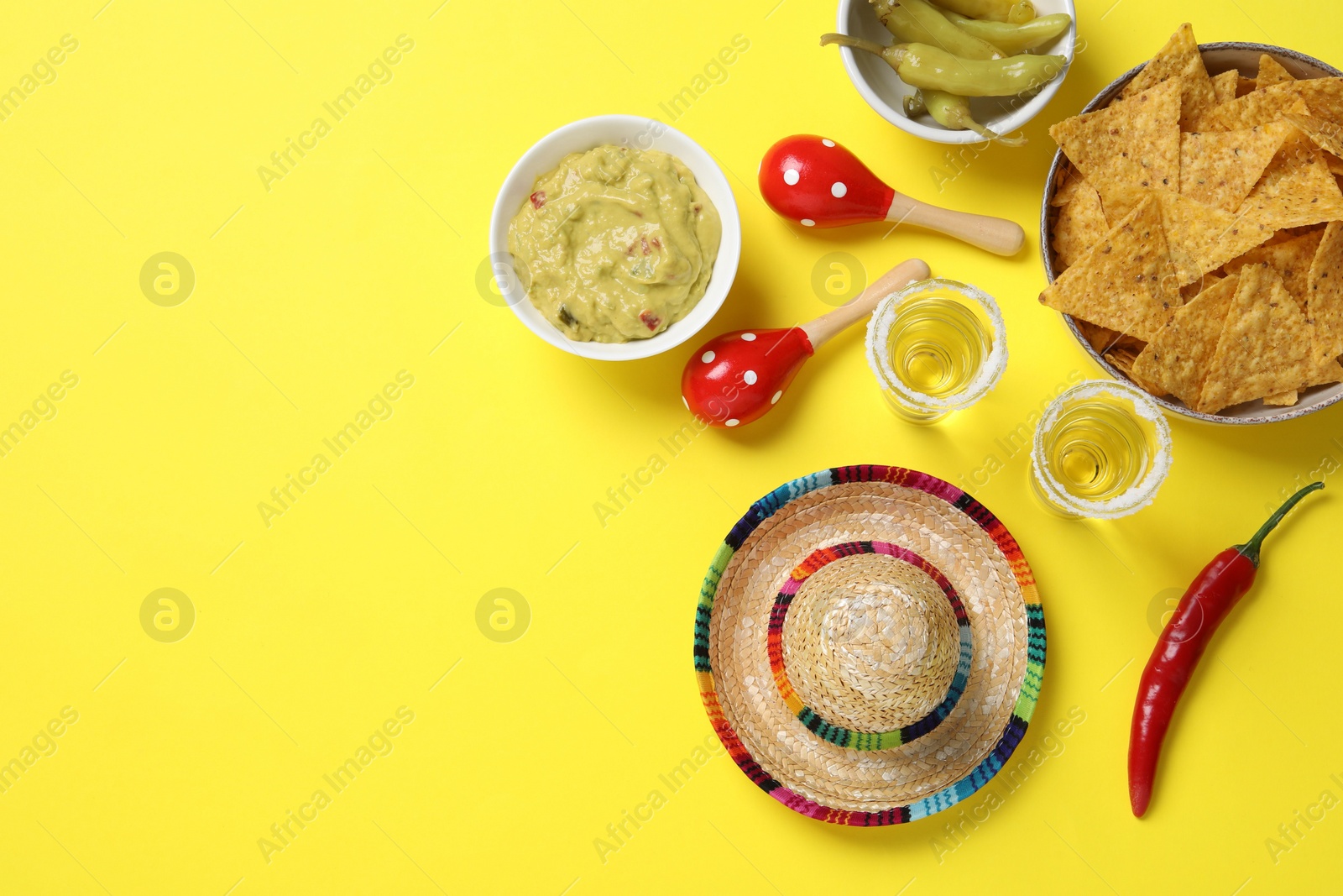 Photo of Mexican sombrero hat, tequila, nachos chips, guacamole and maracas on yellow background, flat lay. Space for text