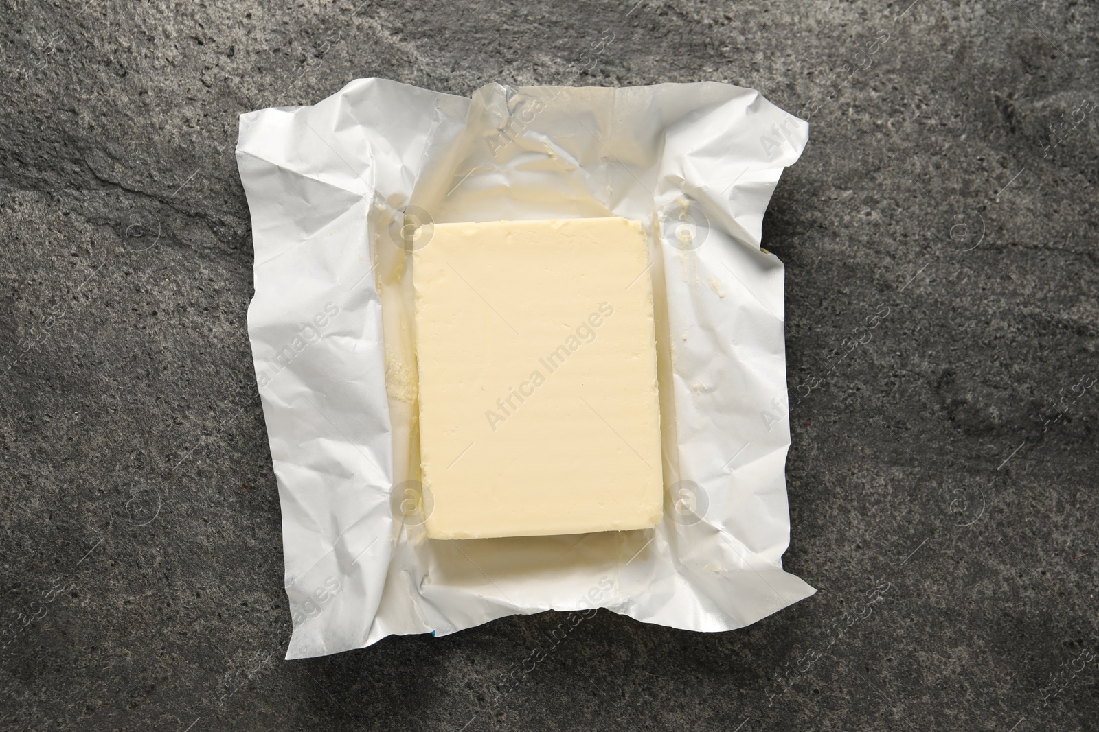 Photo of Block of tasty butter in open foil packaging on grey table, top view