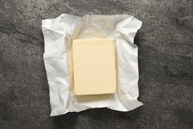 Block of tasty butter in open foil packaging on grey table, top view