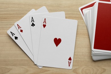 Photo of Four aces and deck of playing cards on wooden table, flat lay