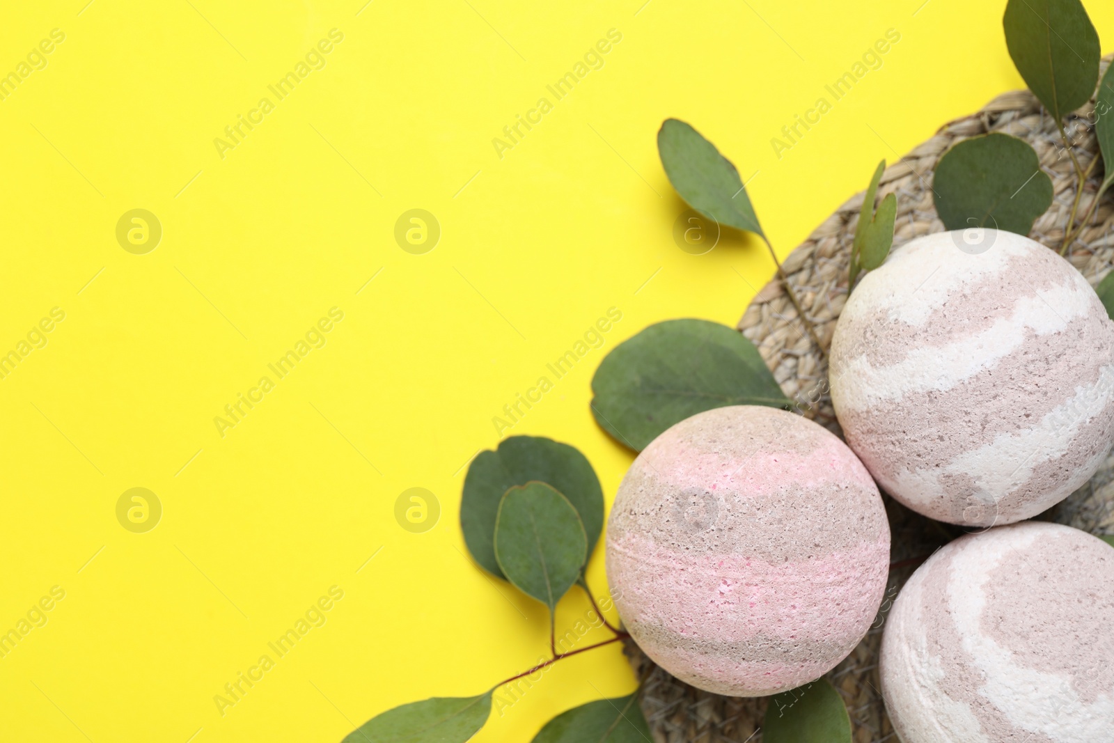 Photo of Bath bombs and eucalyptus leaves on yellow background, flat lay. Space for text