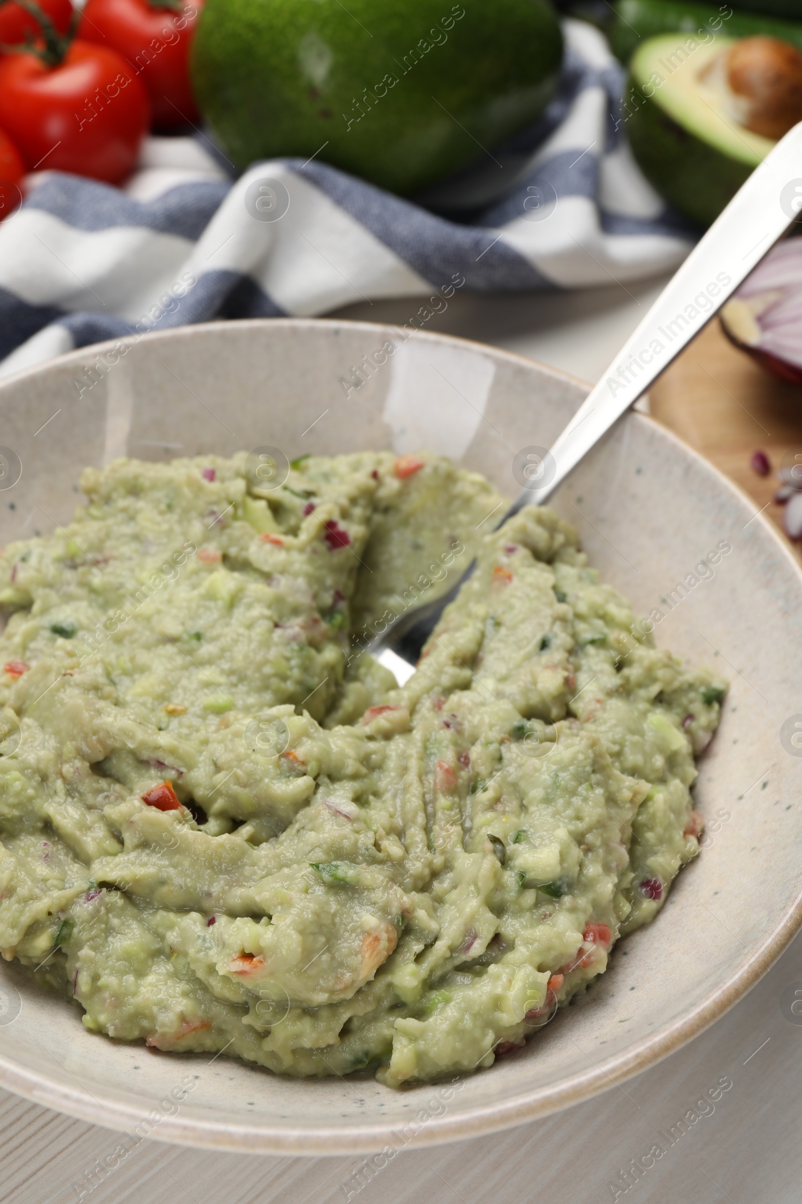 Photo of Preparing delicious guacamole in bowl on white table, closeup