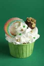 St. Patrick's day party. Tasty cupcake with sour rainbow belt and pot of gold toppers on green background, closeup