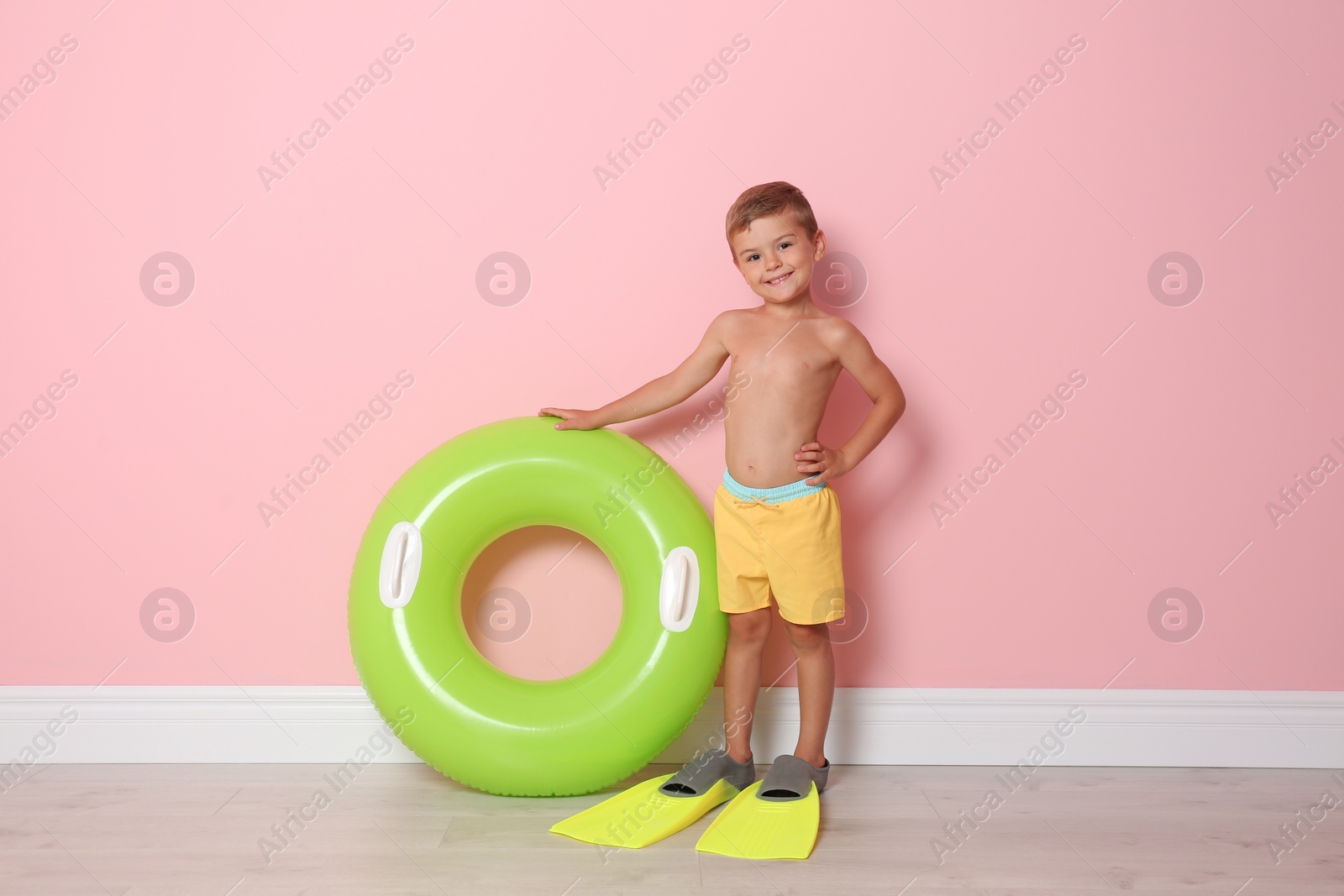 Photo of Cute little boy with inflatable ring wearing flippers near color wall