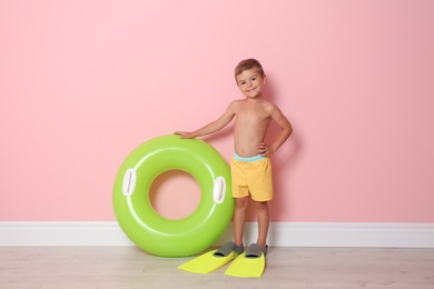 Cute little boy with inflatable ring wearing flippers near color wall