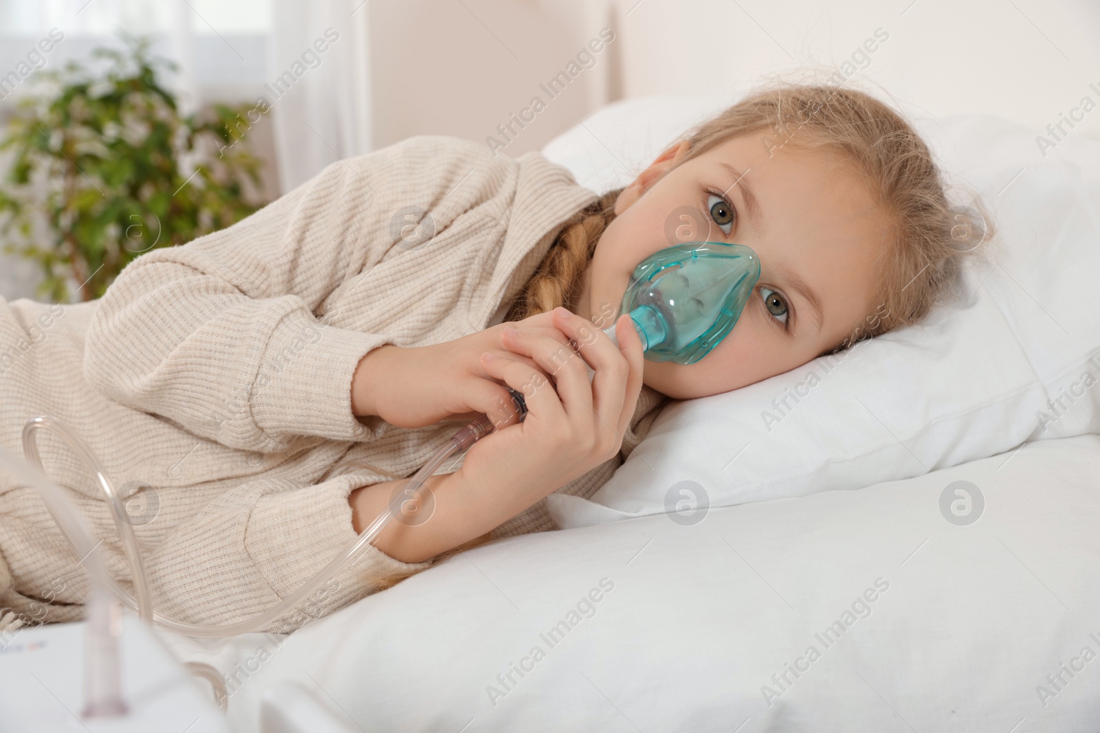 Photo of Little girl using nebulizer for inhalation on bed at home