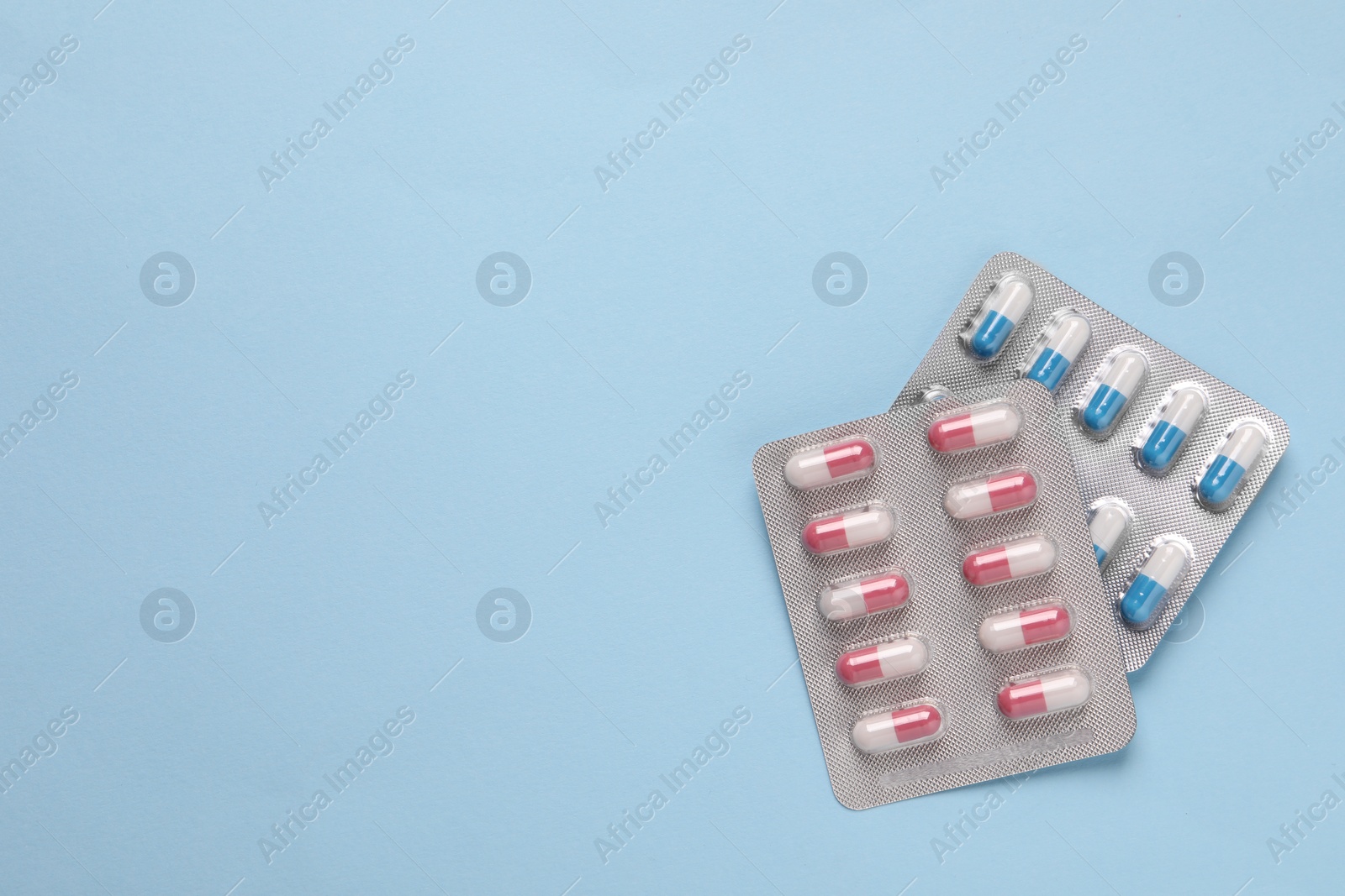 Photo of Pills in blisters on light blue background, top view. Space for text