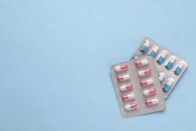 Photo of Pills in blisters on light blue background, top view. Space for text