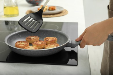 Woman frying delicious cottage cheese pancakes in kitchen, closeup