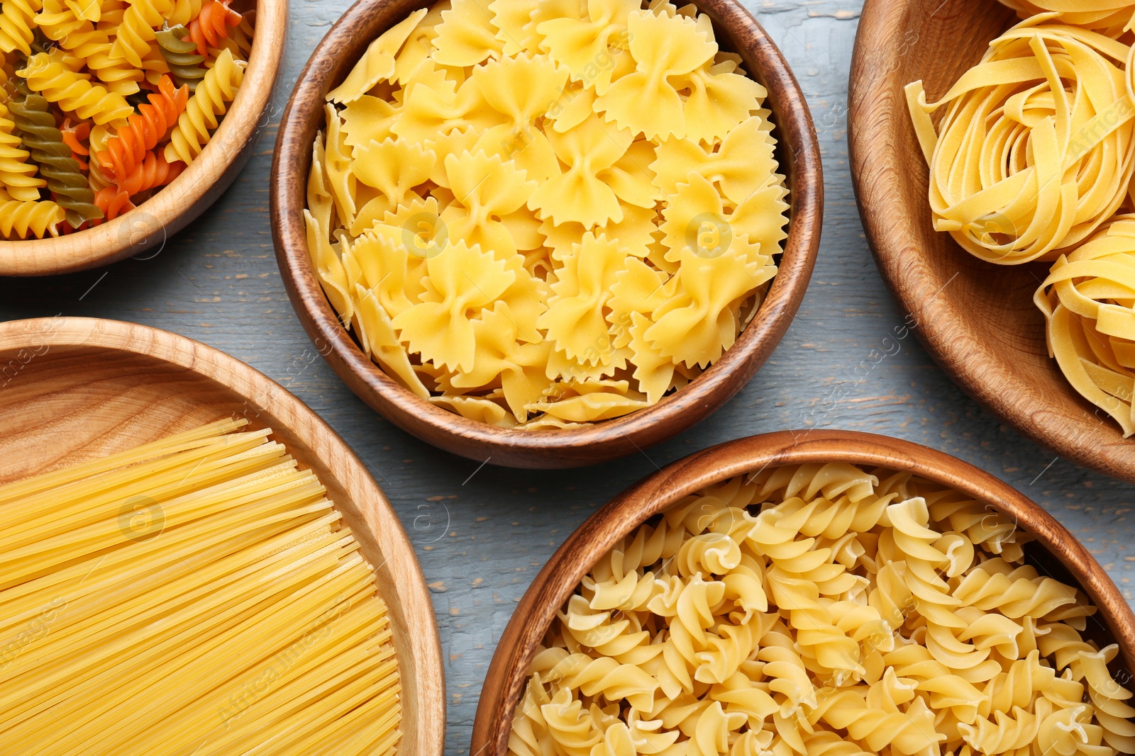 Photo of Different types of pasta on light grey wooden table, flat lay