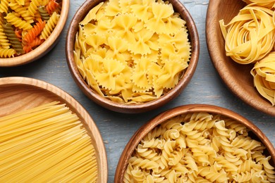 Different types of pasta on light grey wooden table, flat lay