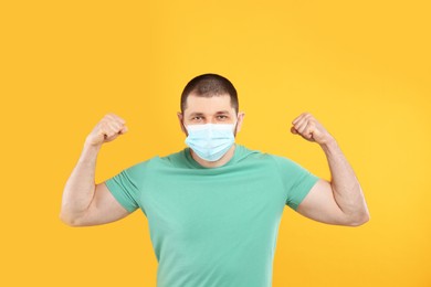 Photo of Man with protective mask showing muscles on yellow background. Strong immunity concept