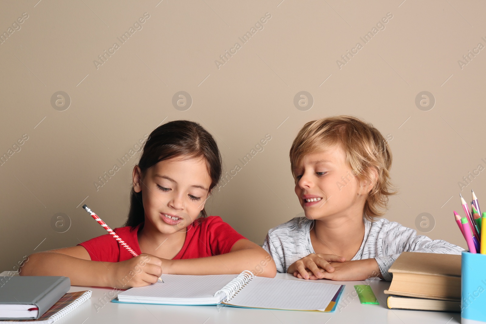 Photo of Little boy and girl doing homework at table on beige background