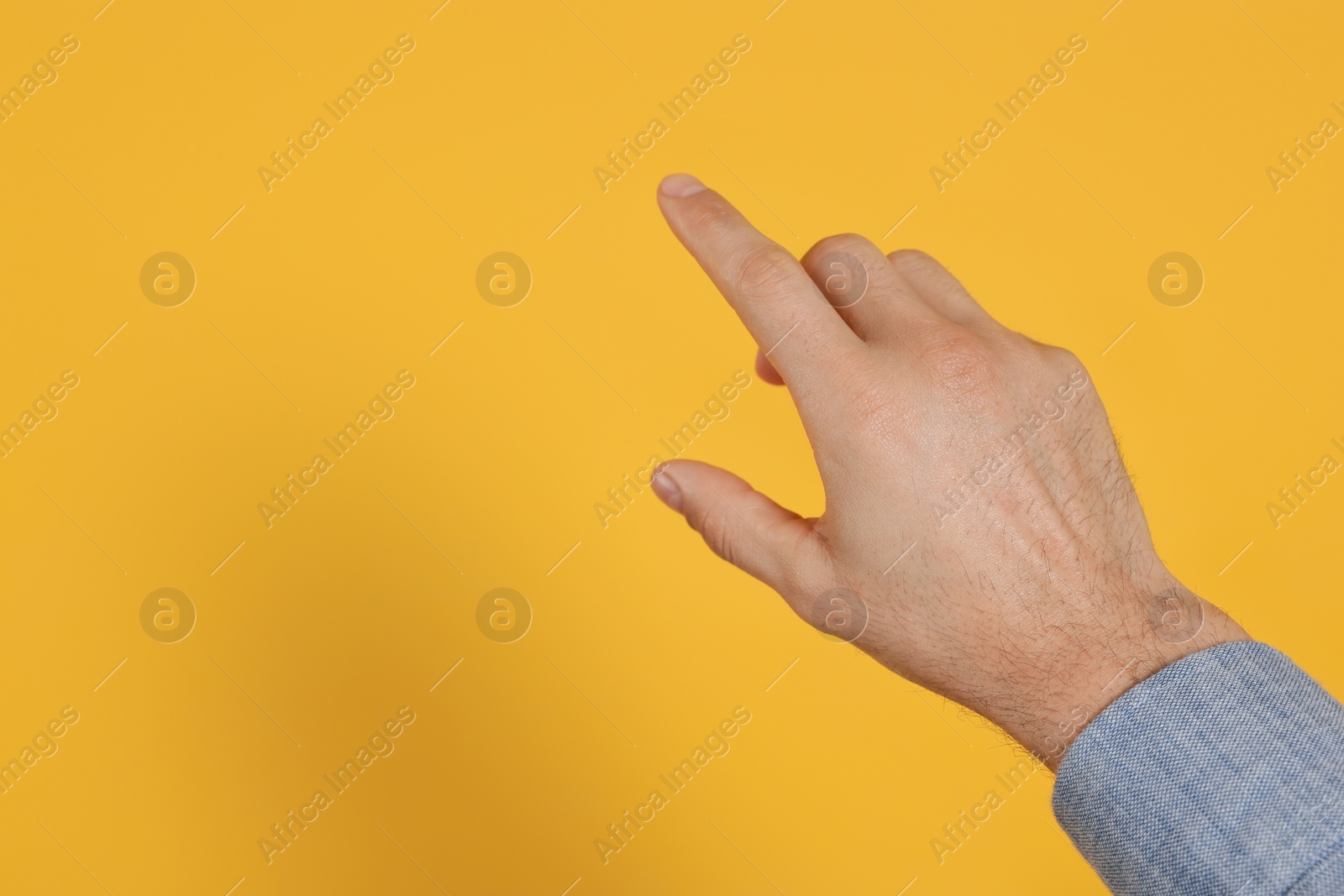 Photo of Man pointing at something against yellow background, closeup on hand. Space for text