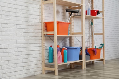 Wooden shelving units with cleaning equipment near white brick wall. Stylish room interior