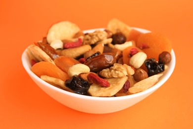 Photo of Bowl with mixed dried fruits and nuts on orange background, closeup