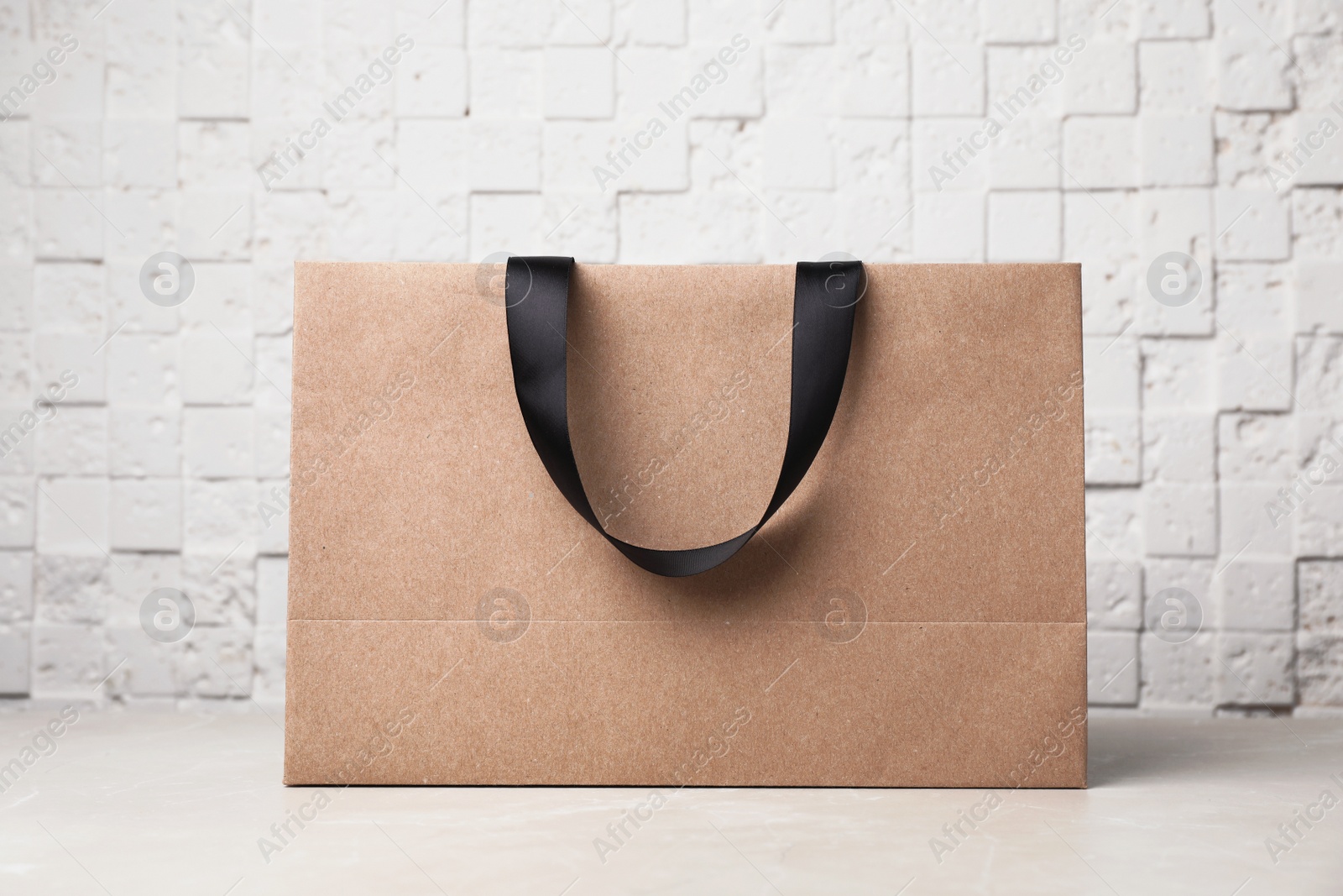 Photo of Paper shopping bag with ribbon handles on table near white wall. Mockup for design