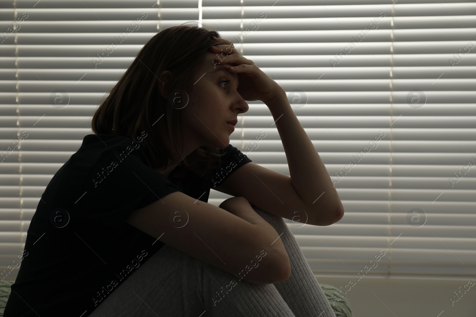 Photo of Sad young woman near window indoors, space for text