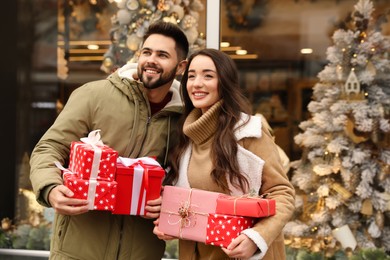 Photo of Lovely couple with presents near store decorated for Christmas outdoors