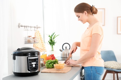 Young woman preparing food near modern multi cooker in kitchen