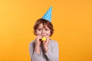 Photo of Birthday celebration. Cute little boy in party hat with blower on orange background