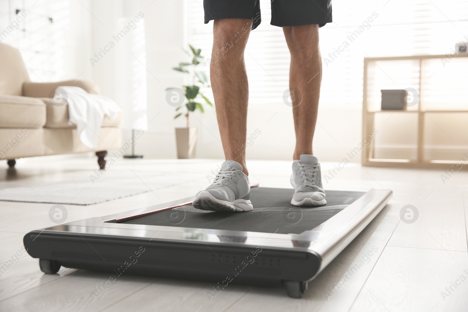 Photo of Sporty man training on walking treadmill at home, closeup