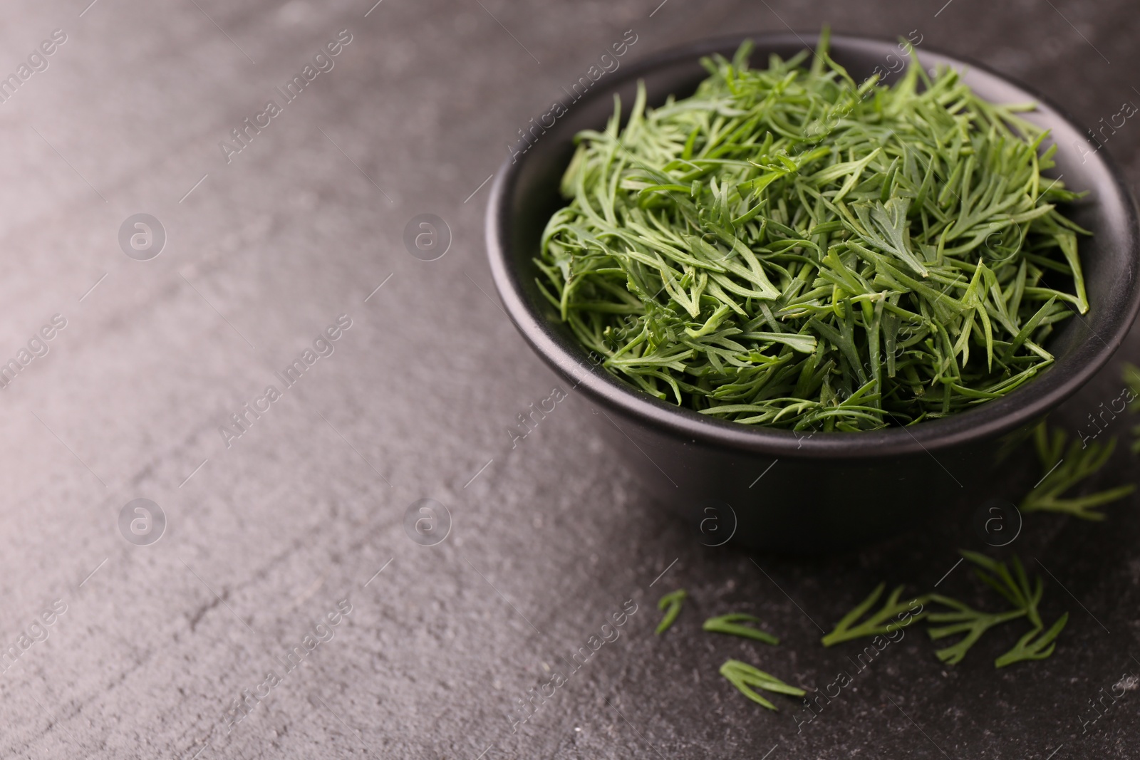 Photo of Fresh cut dill in bowl on dark textured table, closeup. Space for text