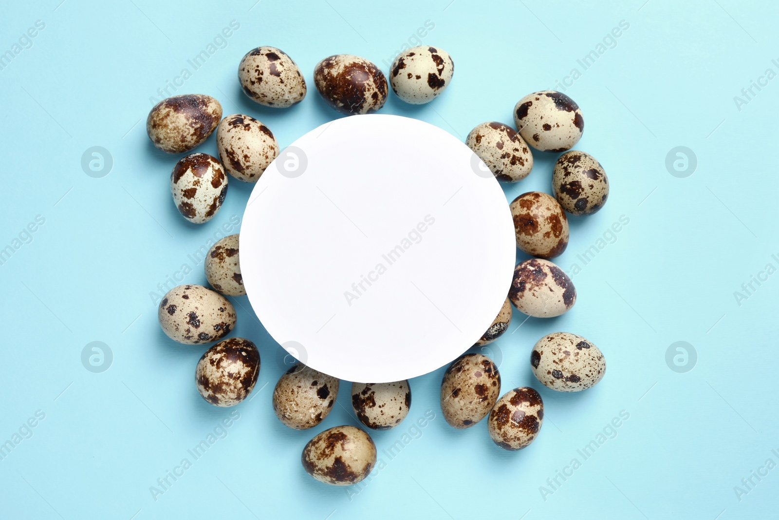 Photo of Speckled quail eggs and blank card on light blue background, top view. Space for text