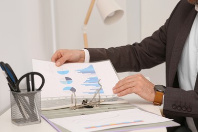 Photo of Businessman putting document into file folder at white table in 'office, closeup