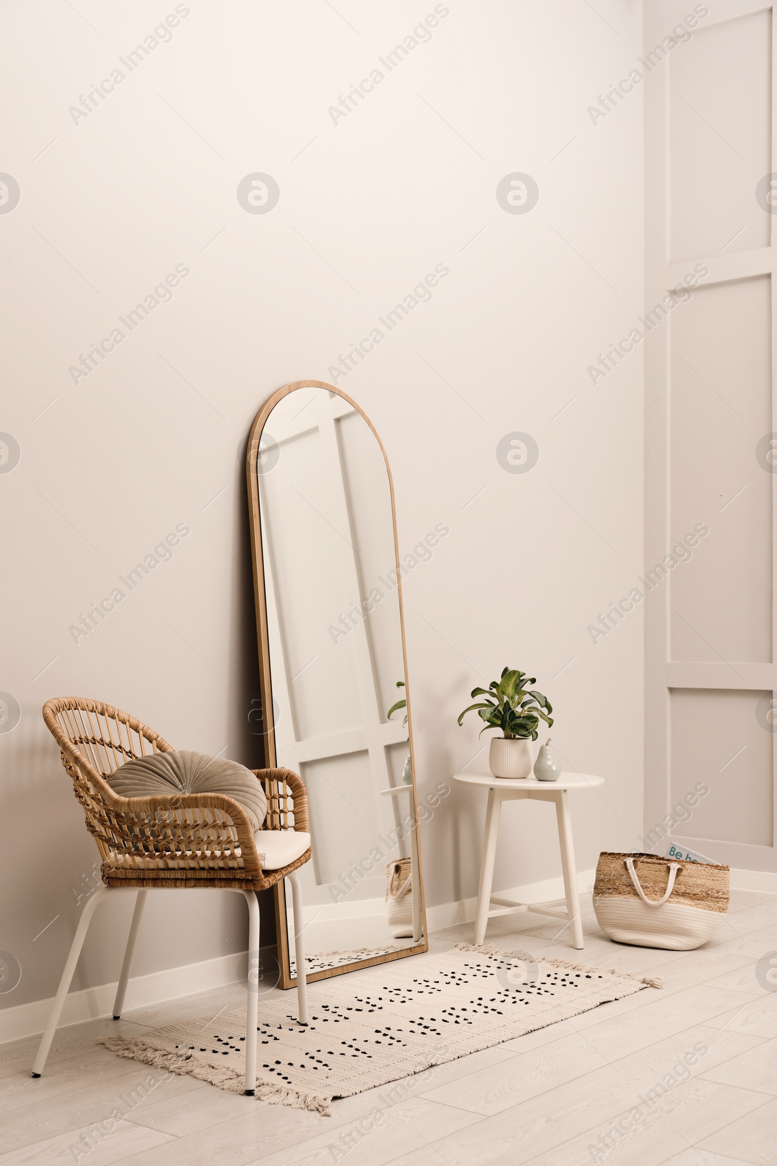 Photo of Beautiful mirror, armchair and plant near white wall indoors. Interior design