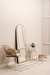 Beautiful mirror, armchair and plant near white wall indoors. Interior design