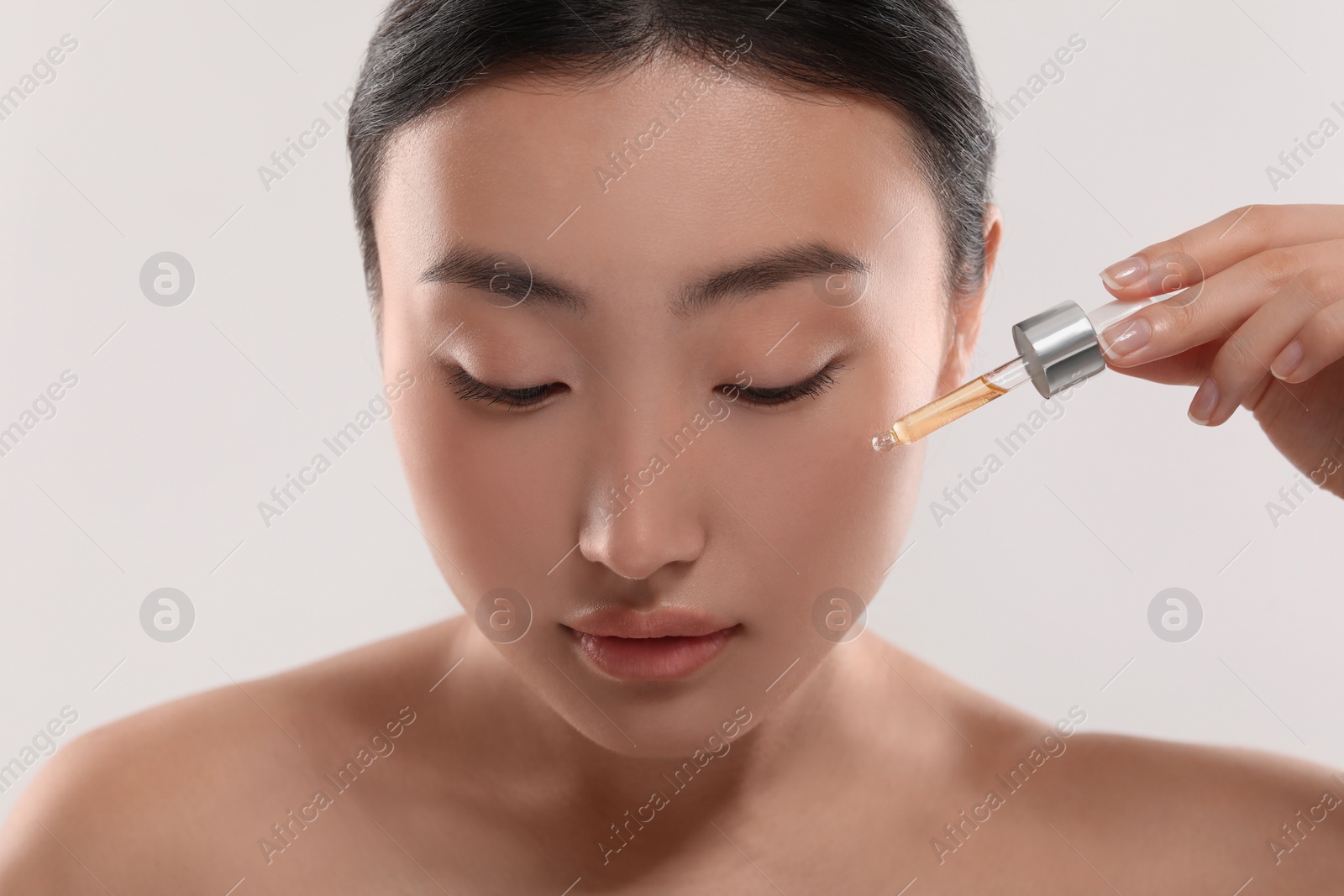 Photo of Beautiful young woman applying cosmetic serum onto her face on white background, closeup