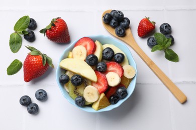 Photo of Tasty fruit salad in bowl and ingredients on white tiled table, flat lay