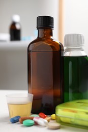 Photo of Bottles of syrup, measuring cup and pills on table. Cold medicine