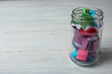 Photo of Glass jar with colorful paper pieces on white wooden table, space for text
