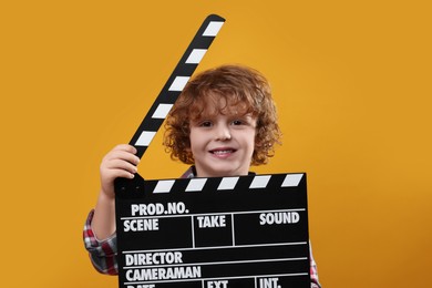 Photo of Smiling cute boy with clapperboard on orange background. Little actor