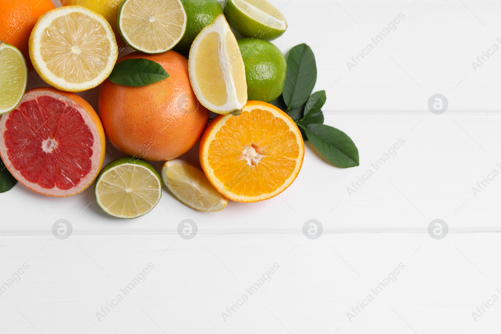 Photo of Different fresh citrus fruits and leaves on white wooden table, flat lay. Space for text