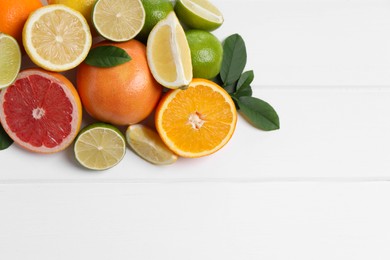 Different fresh citrus fruits and leaves on white wooden table, flat lay. Space for text