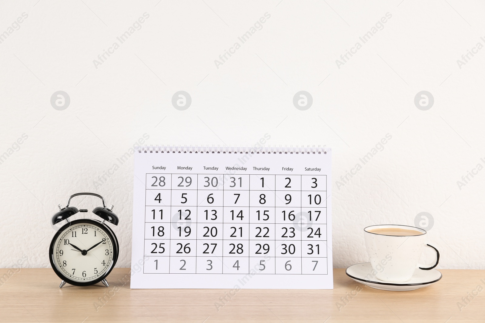 Photo of Calendar, alarm clock and cup of coffee on wooden table