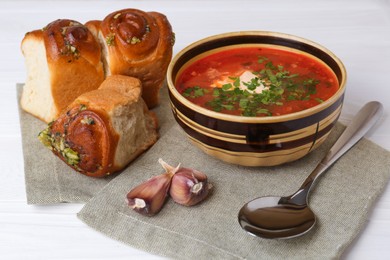 Photo of Delicious borsch served with pampushky on white wooden table. Traditional Ukrainian cuisine