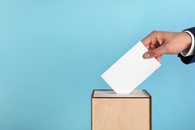 Photo of Man putting his vote into ballot box on light blue background, closeup. Space for text