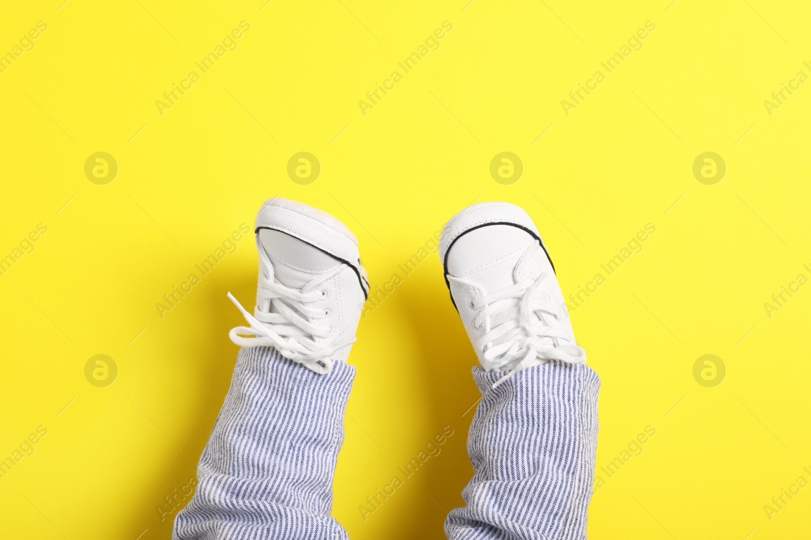 Photo of Little baby in stylish gumshoes on yellow background, top view. Space for text