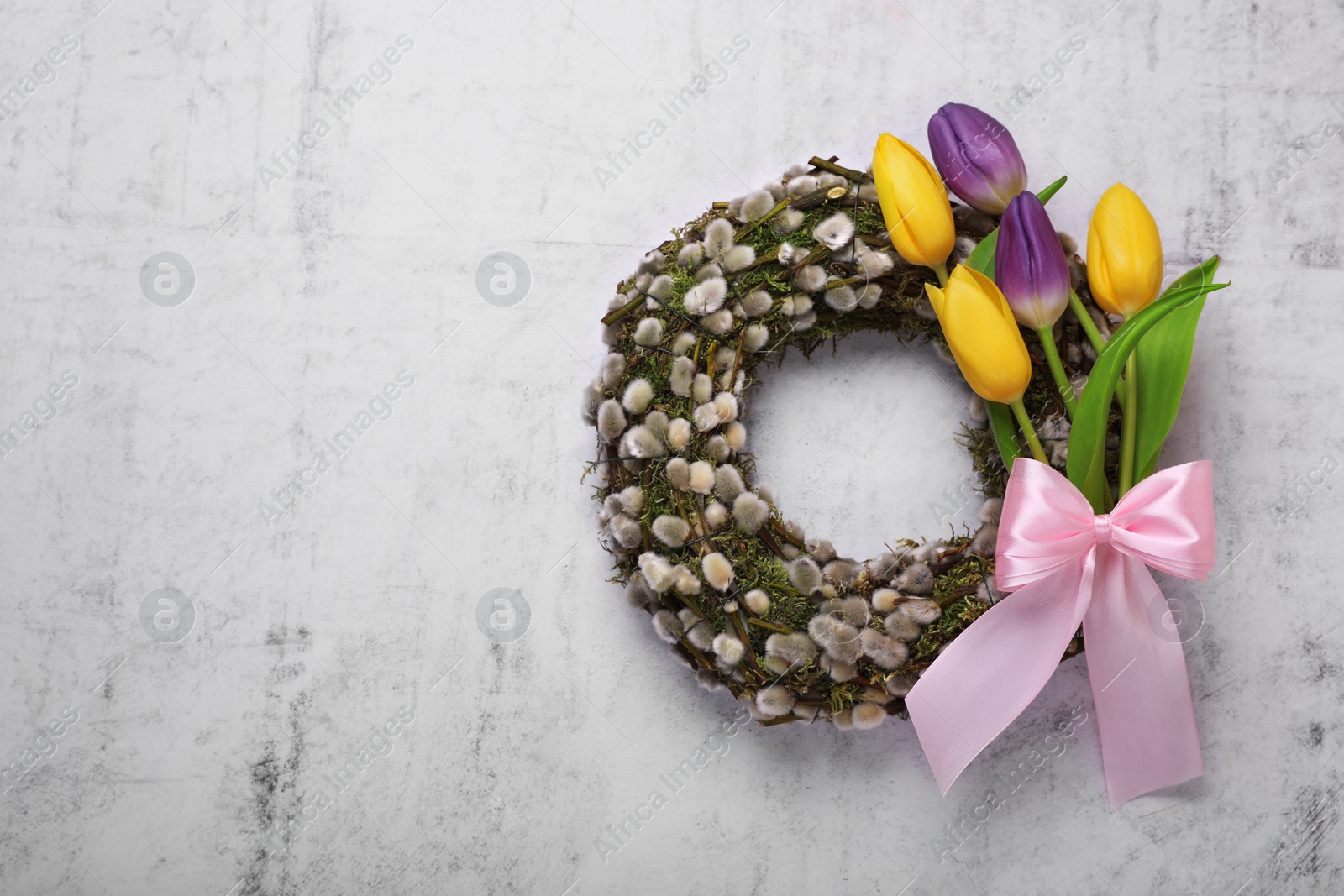 Photo of Wreath made of beautiful willow, colorful tulip flowers and pink bow on light background, top view. Space for text