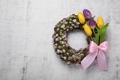 Wreath made of beautiful willow, colorful tulip flowers and pink bow on light background, top view. Space for text