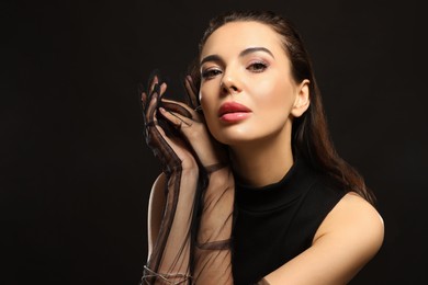 Portrait of beautiful young woman in elegant evening gloves on black background