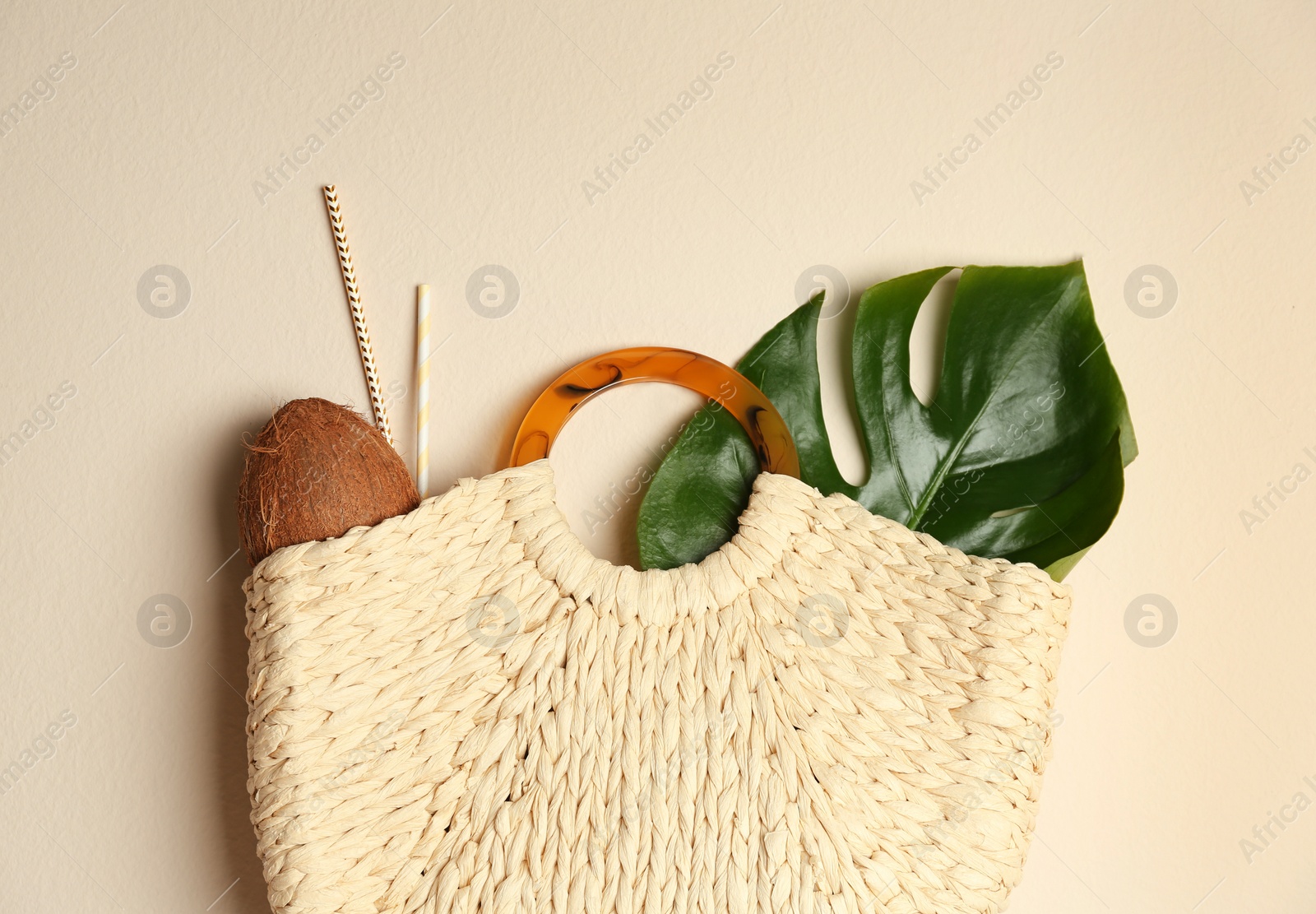 Photo of Elegant woman's straw bag with coconut, tropical leaf and straws on beige background, top view