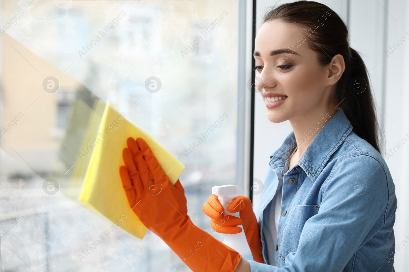 Image of Young woman wiping window glass with rag at home. Cleaning service 