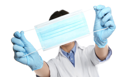 Photo of Doctor in latex gloves holding disposable face mask on white background, closeup. Protective measures during coronavirus quarantine