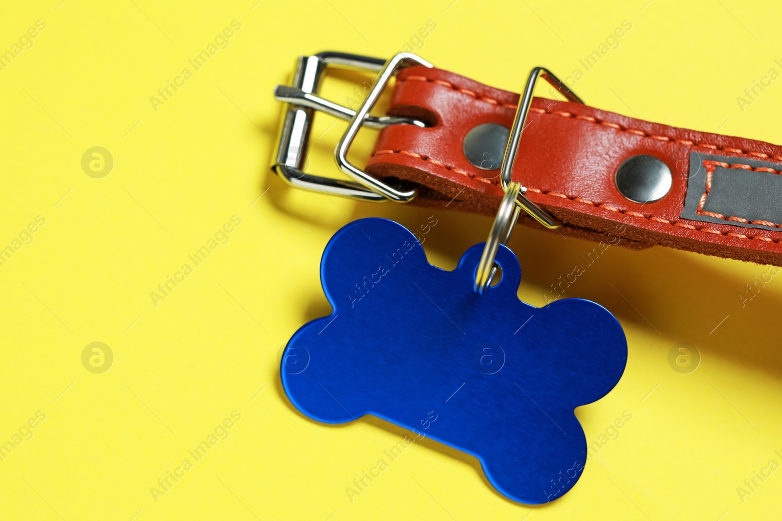 Photo of Leather dog collar with blue tag in shape of bone on yellow background, closeup. Space for text